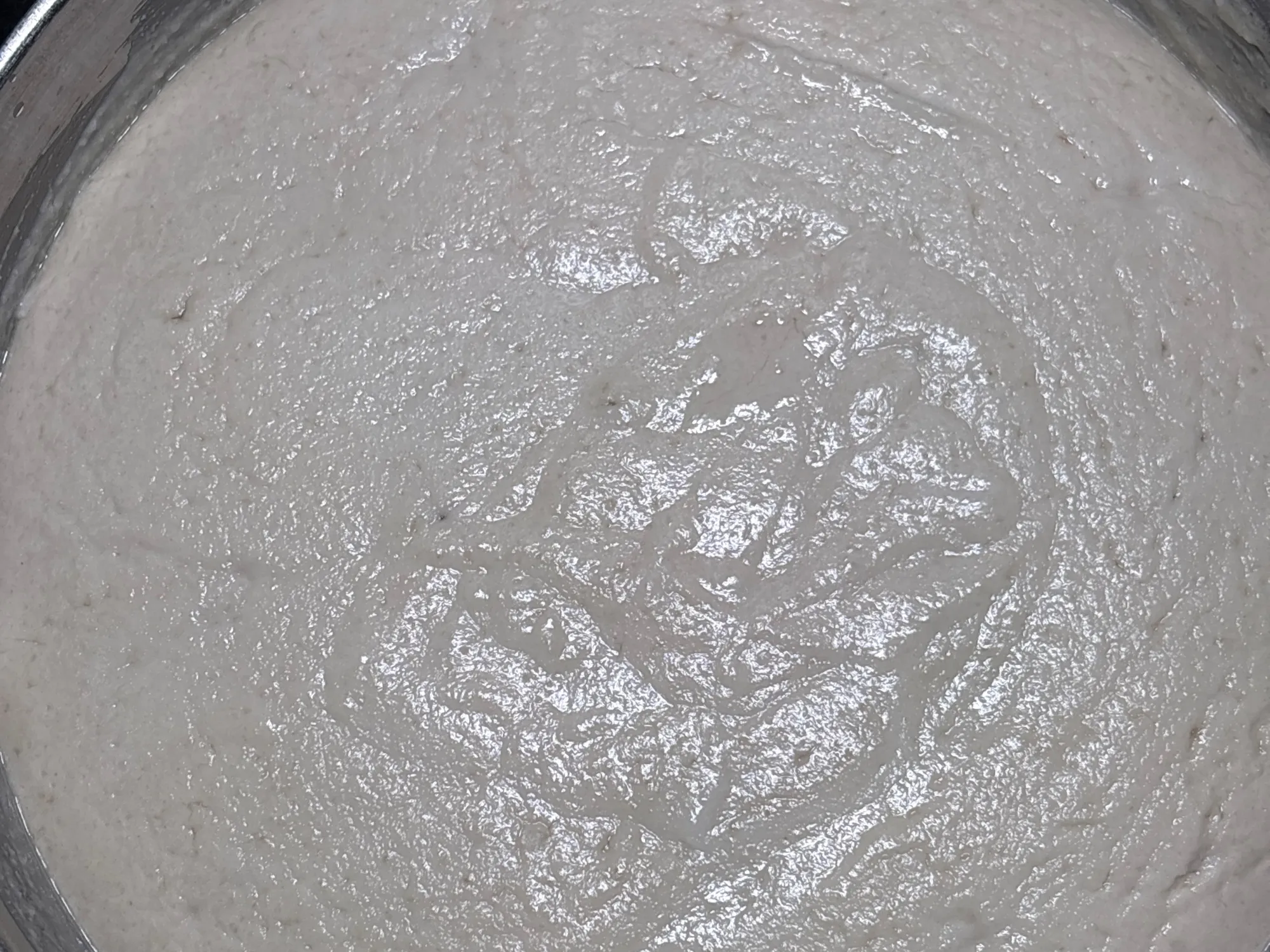 A steel vessel of risen, bubbled batter with a ladle in it, beside a plate of idlis and a folded dosa