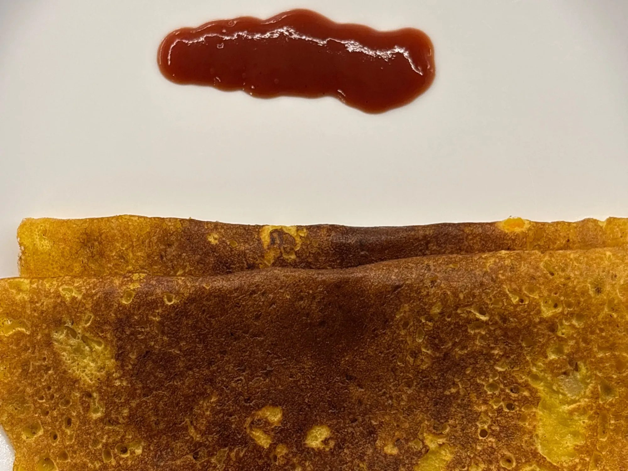 A yellow pancake on a tawa flecked with orange carrot and green coriander, edges lifting and crisp